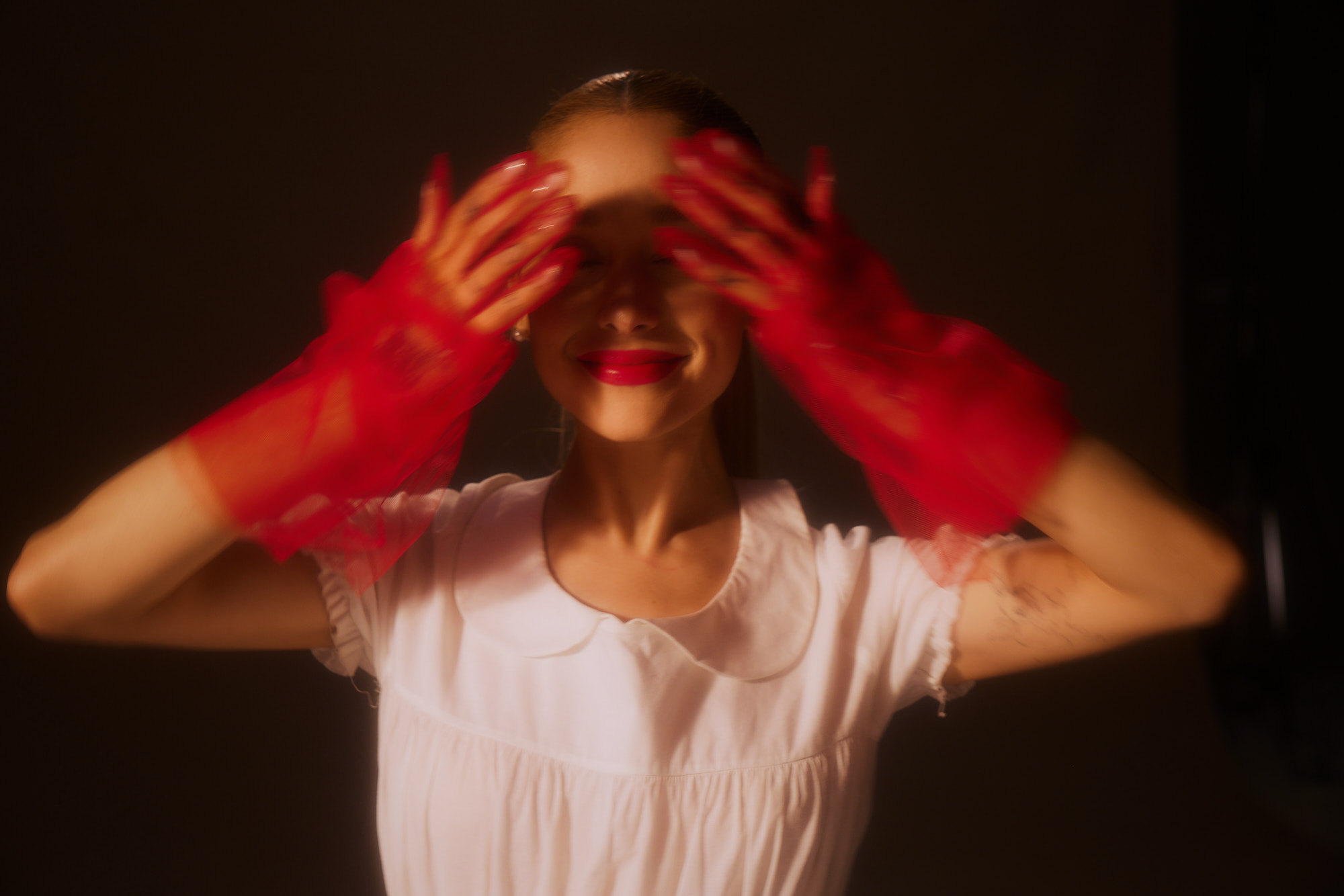 the red of the gloves, paired with the innocent white dress, echoes a juxtaposition of passion and purity. meanwhile The dark background augments the sense of mesmerizing self-revelation.