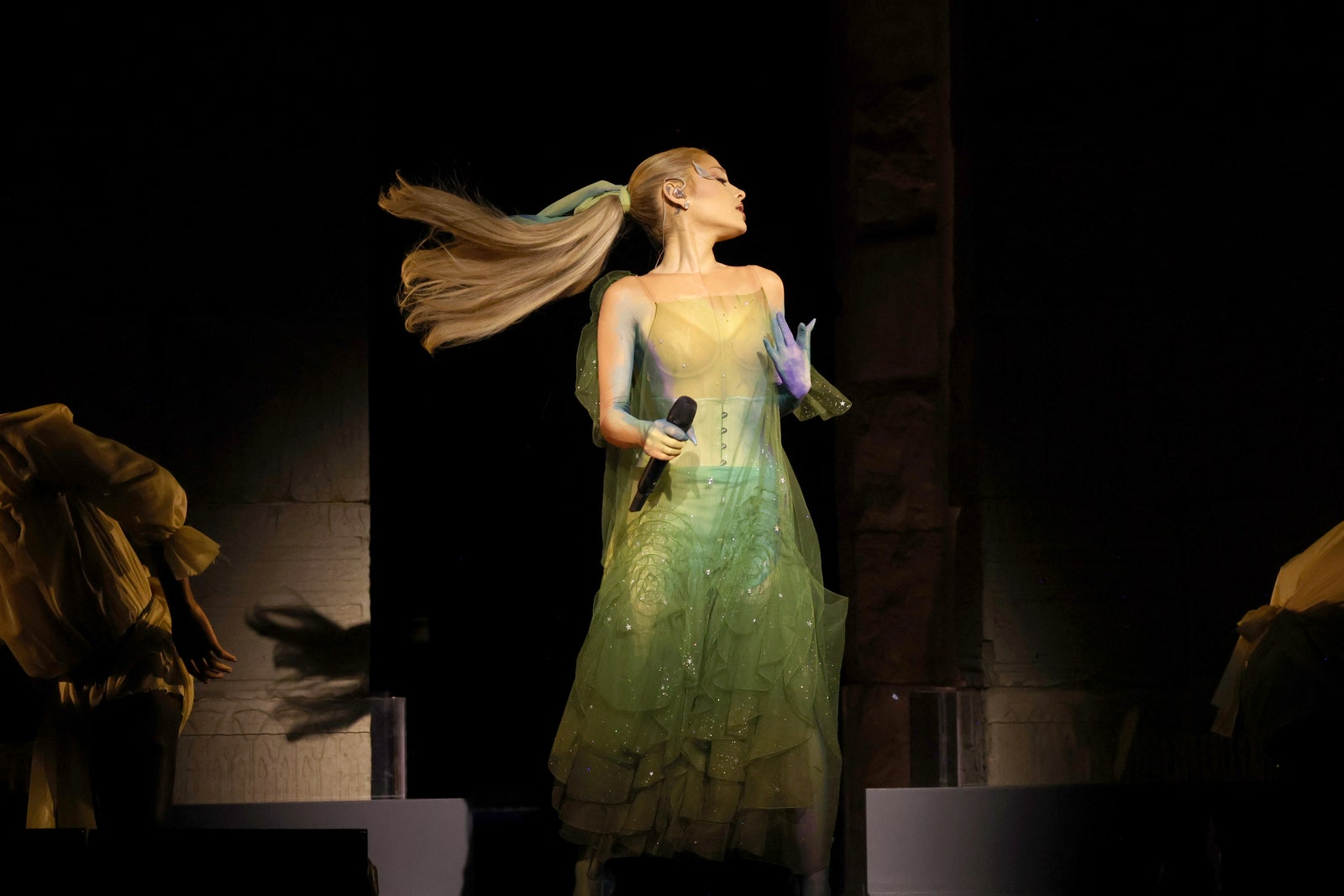 Ariana Grande in a mesmerizing sheer green Maison Margiela gown designed by John Galliano, glowing as she serenades the audience.